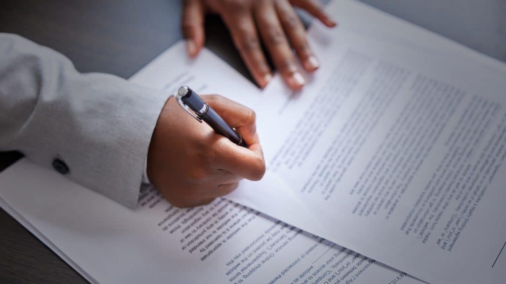 Close up of paperwork, hands, and person signing with a pen.