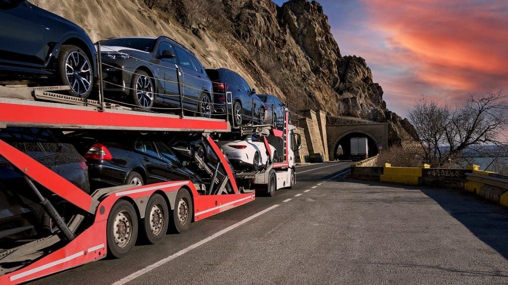 Open trailer hauling several vehicles on a mountain road.