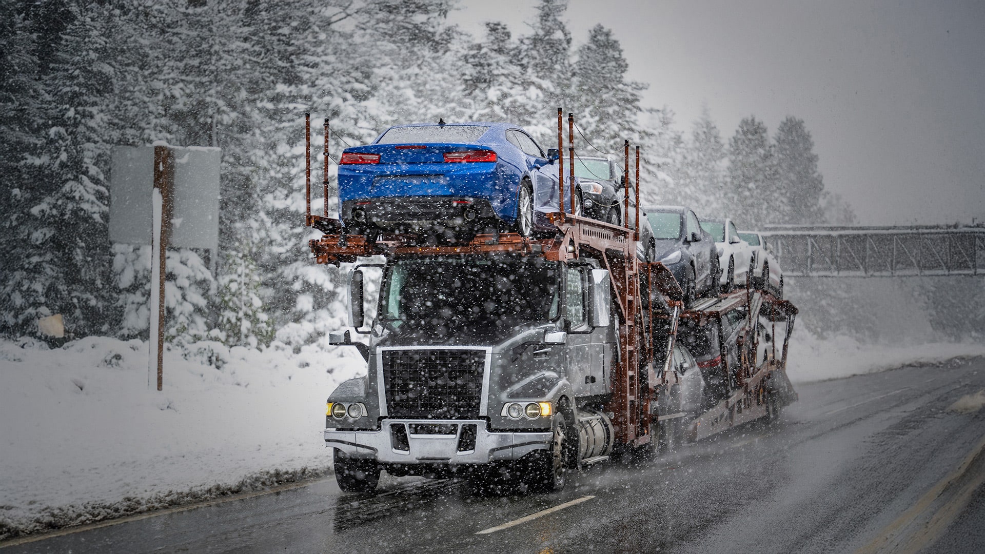 Open transport truck, with multiple vehicles on top in extreme snowy conditions